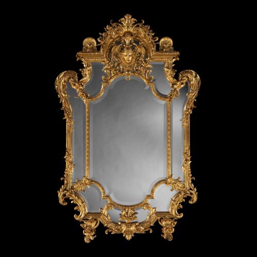 Of generous proportions, with effusive carved details, the central bevelled glass surrounded by an outer reserve of mirrored panels, the frame carved with scrolls, floral garland, pendants below and a mask of Apollo flanked by shells at the crest.