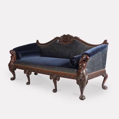 The mahogany settee has the end arm supports carved with recumbent mermaids, terminating in Georgian style 'hairy paw feet', the centre legs carved with winged female herms, and the rear legs carved with acanthus leaves and conforming hairy paw feet; the seat rails carved with a running bead & reel design, and acanthus leaves; the top rail having a fine carved central medallion motif of Venus and Cupid, flanked with egg-and dart scrolls.