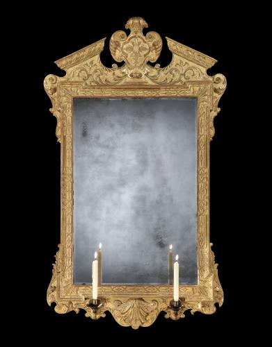 A rectangular gilt mirror, with top cresting of cartouche within a broken pediment and at the bottom in the classic stylised shell shape. Also at the bottom of the mirror frame, there are two brass candle arms fitted with two wax candles. 
